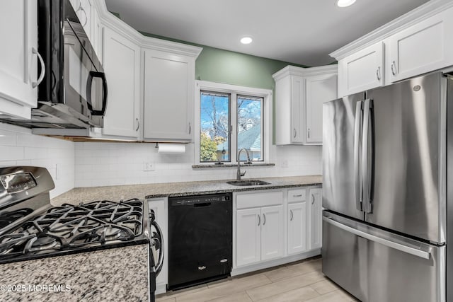 kitchen with black appliances, a sink, backsplash, white cabinetry, and light stone countertops