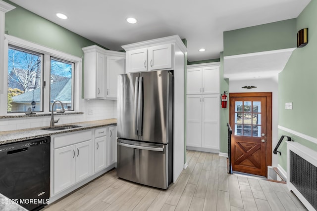 kitchen with freestanding refrigerator, a sink, decorative backsplash, black dishwasher, and white cabinetry