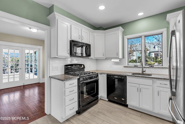 kitchen with stone countertops, a sink, black appliances, white cabinetry, and tasteful backsplash