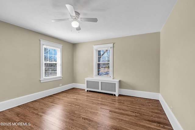 unfurnished room with a ceiling fan, radiator heating unit, wood finished floors, and baseboards