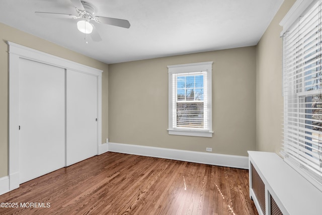 unfurnished bedroom featuring a closet, baseboards, wood finished floors, and a ceiling fan