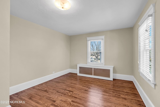 spare room featuring baseboards, radiator, and wood finished floors