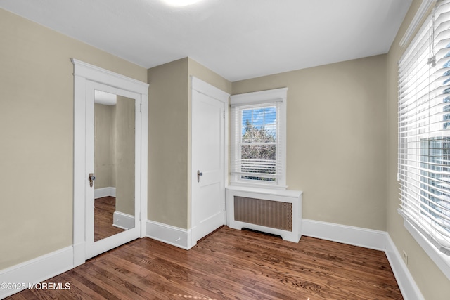 unfurnished bedroom featuring radiator heating unit, baseboards, and wood finished floors