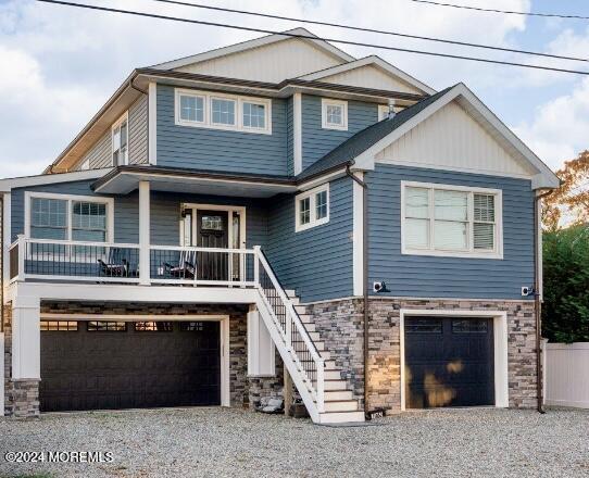 view of front facade with stone siding, a porch, stairway, gravel driveway, and an attached garage