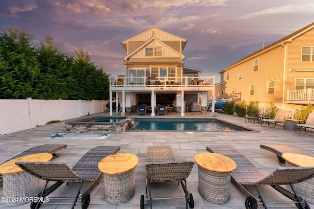 rear view of property with a patio, a balcony, a fenced backyard, and a pool with connected hot tub