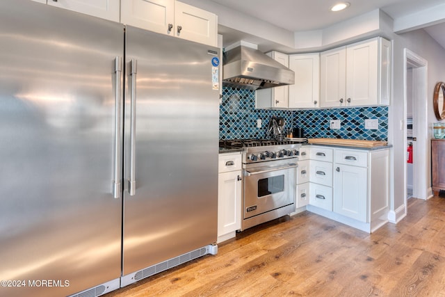 kitchen with light wood finished floors, decorative backsplash, white cabinetry, wall chimney range hood, and high quality appliances