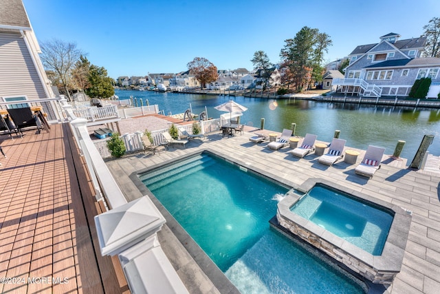 view of pool featuring fence, a pool with connected hot tub, a water view, a patio area, and a residential view