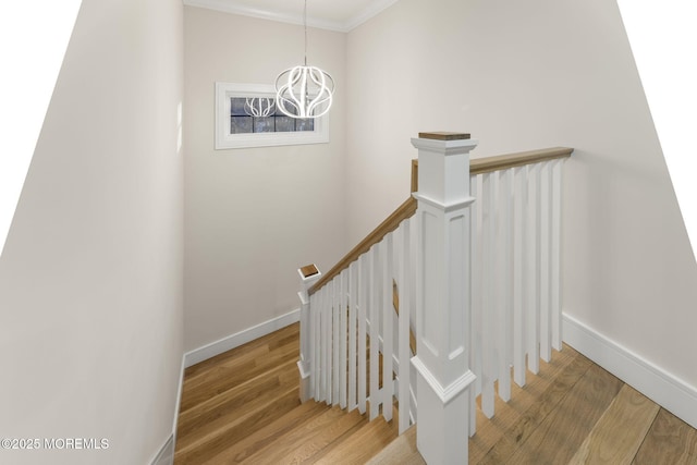 stairs with baseboards, a notable chandelier, wood finished floors, and crown molding