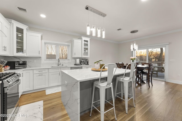 kitchen with tasteful backsplash, a breakfast bar area, light wood-style flooring, stainless steel gas stove, and a sink