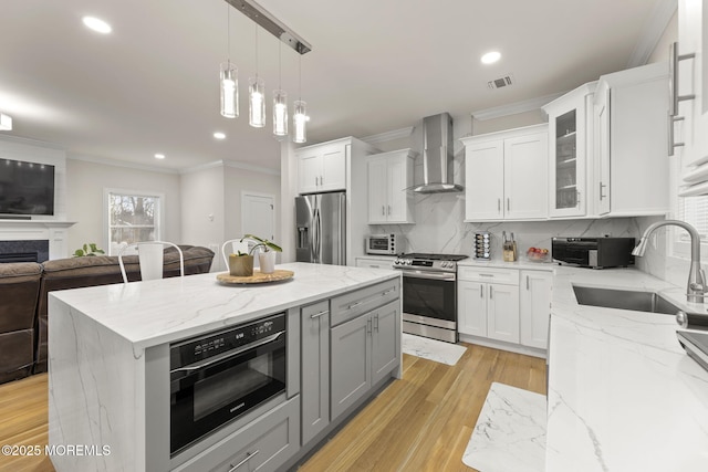 kitchen with visible vents, gray cabinetry, a sink, appliances with stainless steel finishes, and wall chimney exhaust hood