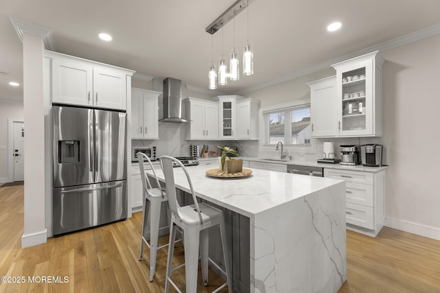 kitchen with appliances with stainless steel finishes, ornamental molding, and wall chimney range hood