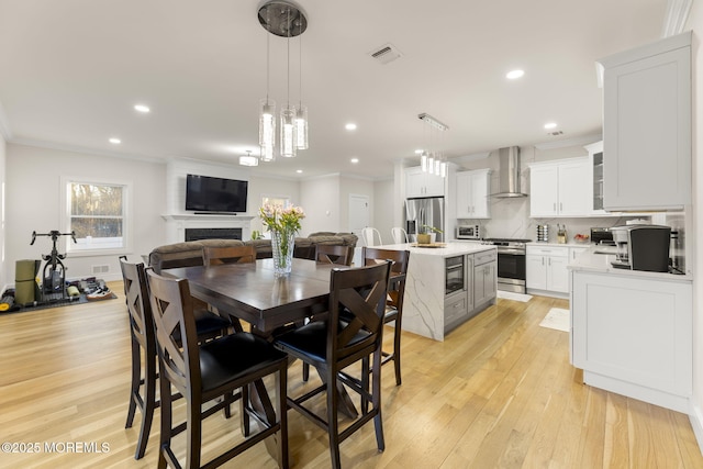 dining space featuring visible vents, ornamental molding, recessed lighting, light wood-style flooring, and a fireplace