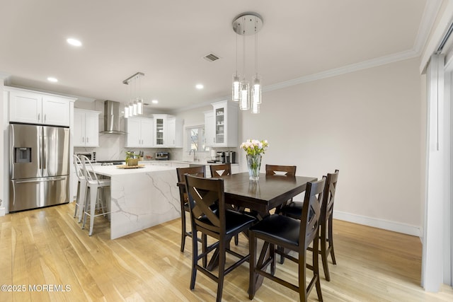 dining room featuring visible vents, baseboards, light wood-style flooring, and crown molding