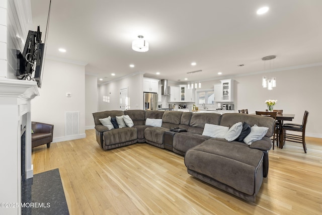 living room with baseboards, visible vents, light wood-style flooring, a fireplace with flush hearth, and ornamental molding