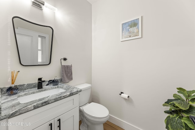 bathroom featuring baseboards, toilet, wood finished floors, and vanity