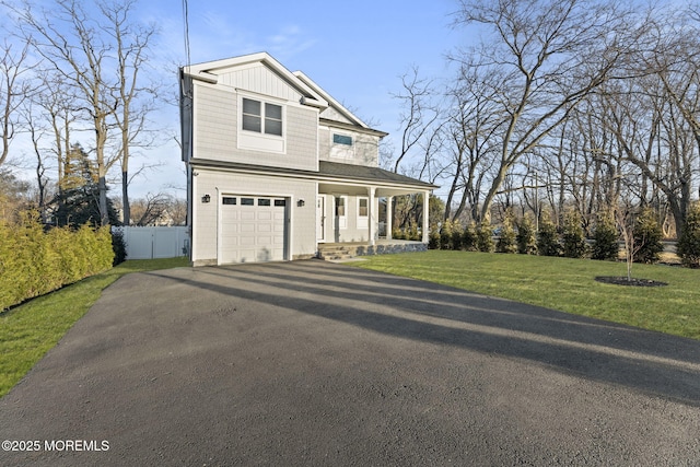 view of front of property featuring board and batten siding, a front lawn, fence, covered porch, and driveway