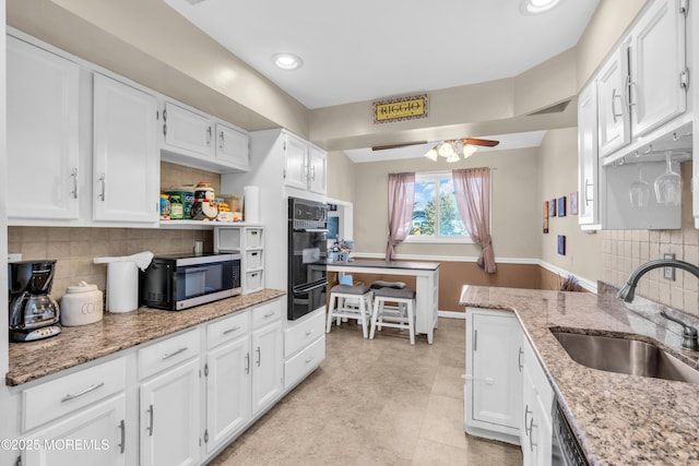 kitchen featuring a warming drawer, a sink, white cabinetry, light stone countertops, and ceiling fan