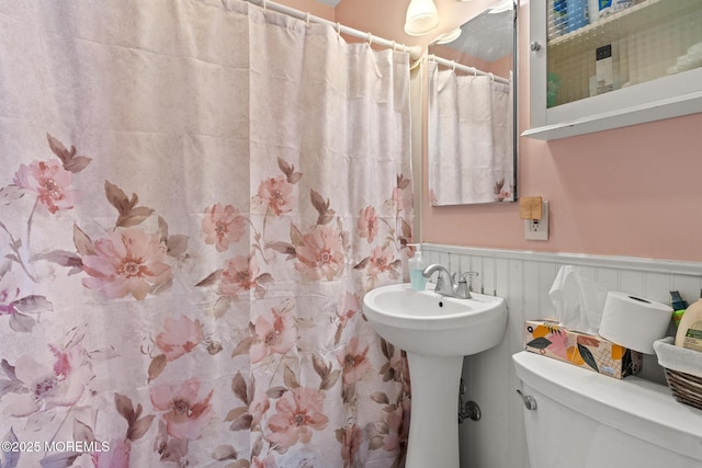 bathroom with a wainscoted wall, curtained shower, toilet, and a sink