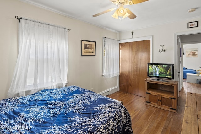 bedroom featuring wood finished floors, a ceiling fan, ornamental molding, a closet, and a baseboard heating unit