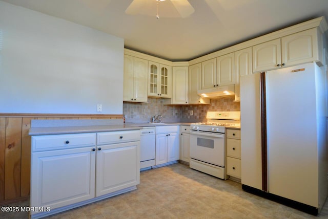 kitchen featuring under cabinet range hood, light countertops, wainscoting, white appliances, and a sink