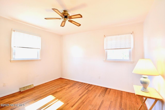 unfurnished room with a ceiling fan, wood finished floors, visible vents, and baseboards