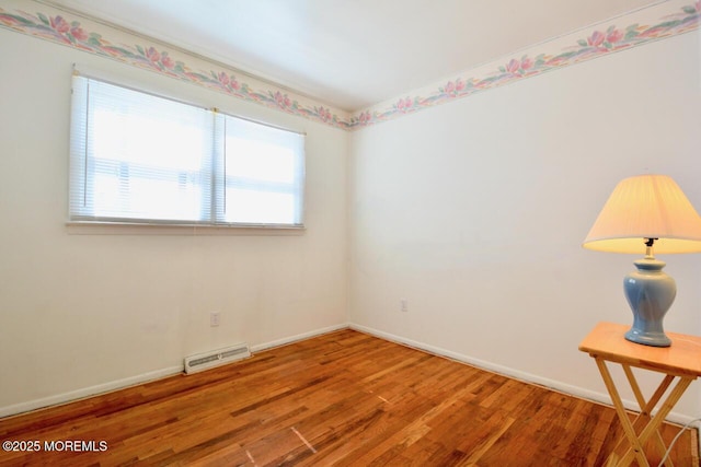 spare room featuring visible vents, baseboards, and wood finished floors