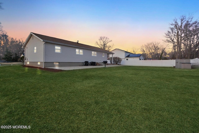 back of property at dusk with a patio, a yard, and fence