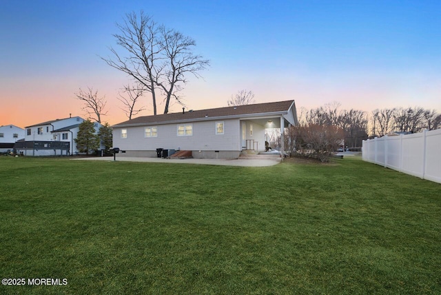 back of house at dusk with crawl space, a yard, and fence