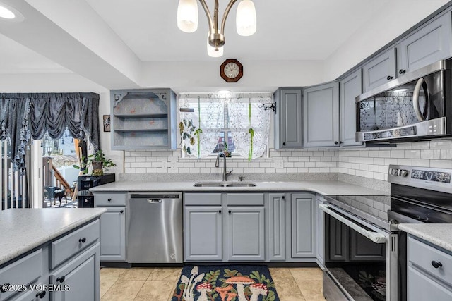 kitchen with light countertops, decorative backsplash, gray cabinets, appliances with stainless steel finishes, and a sink