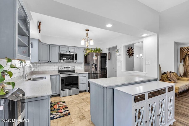 kitchen featuring tasteful backsplash, gray cabinetry, light countertops, stainless steel appliances, and a sink