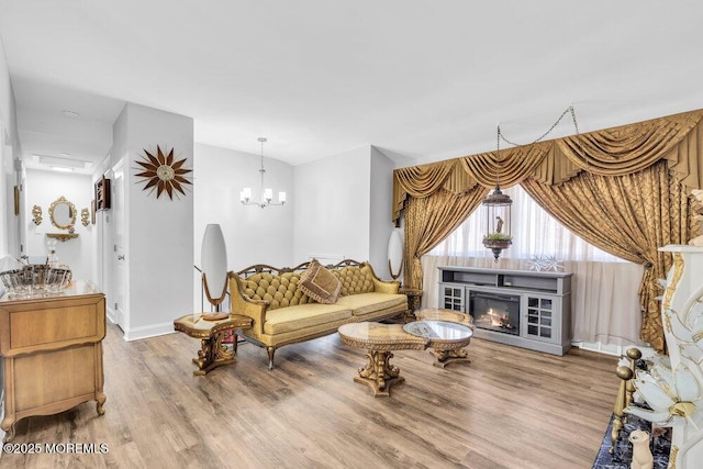 living area featuring baseboards, wood finished floors, an inviting chandelier, and a glass covered fireplace