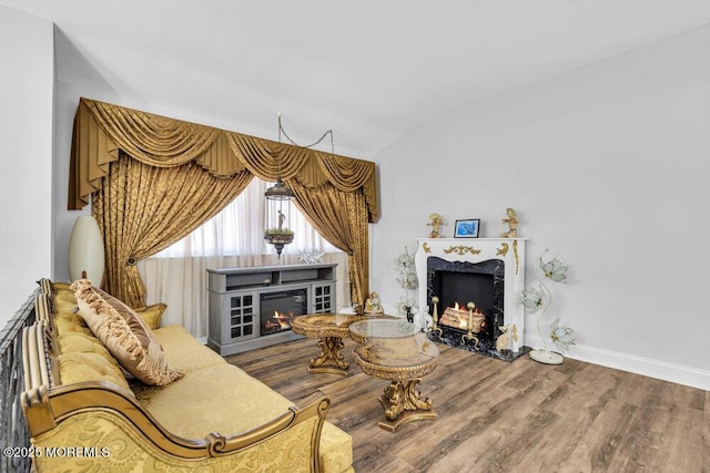 living area with vaulted ceiling, wood finished floors, baseboards, and a high end fireplace