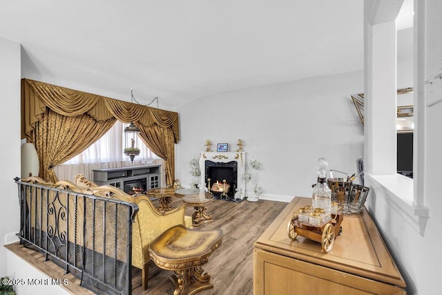 living area featuring baseboards, a warm lit fireplace, wood finished floors, and vaulted ceiling