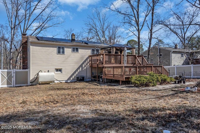 rear view of house featuring solar panels, heating fuel, a fenced backyard, and a wooden deck