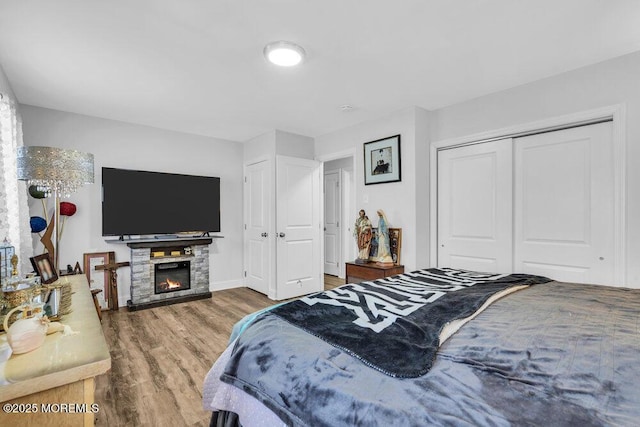 bedroom with a stone fireplace, wood finished floors, and baseboards