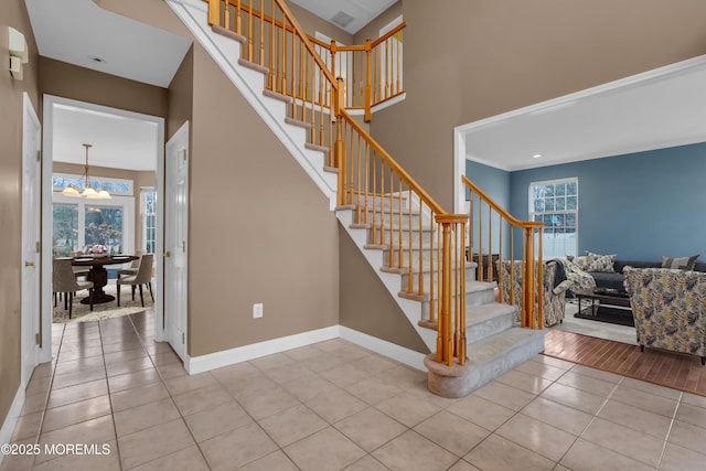 staircase with baseboards, an inviting chandelier, a towering ceiling, and tile patterned flooring