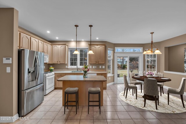 kitchen featuring light brown cabinetry, a sink, a center island, white appliances, and light countertops