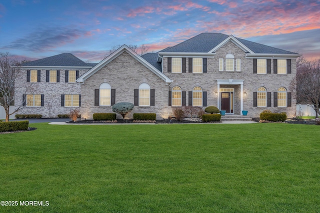 colonial house with a lawn, brick siding, and a shingled roof