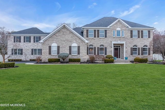 view of front of home with a front lawn, brick siding, and a shingled roof