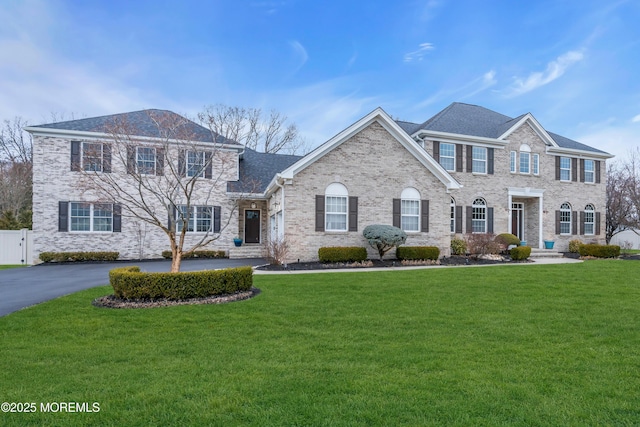 view of front facade featuring brick siding, aphalt driveway, a front yard, and fence