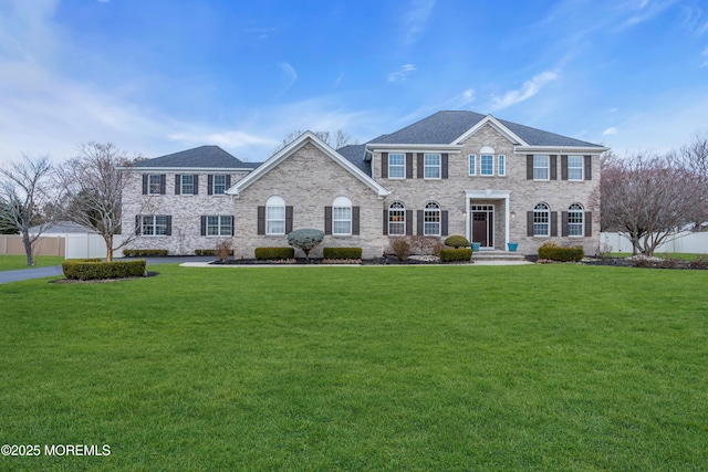 colonial home featuring a front lawn, fence, and brick siding