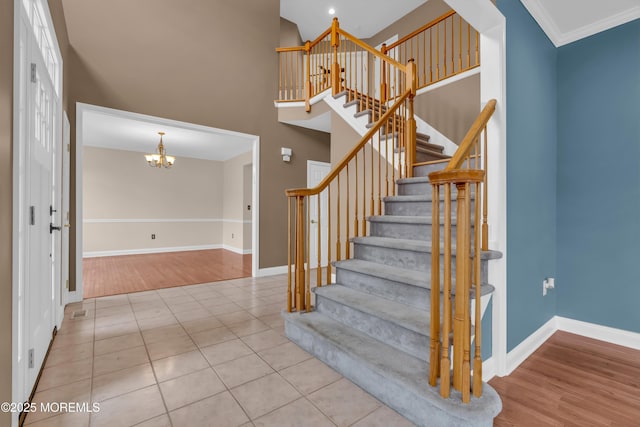 stairs featuring wood finished floors, baseboards, ornamental molding, a towering ceiling, and a notable chandelier