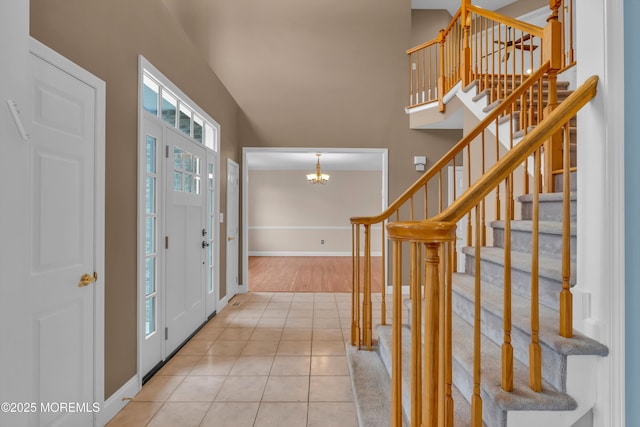 tiled foyer entrance featuring stairs, a high ceiling, baseboards, and a chandelier