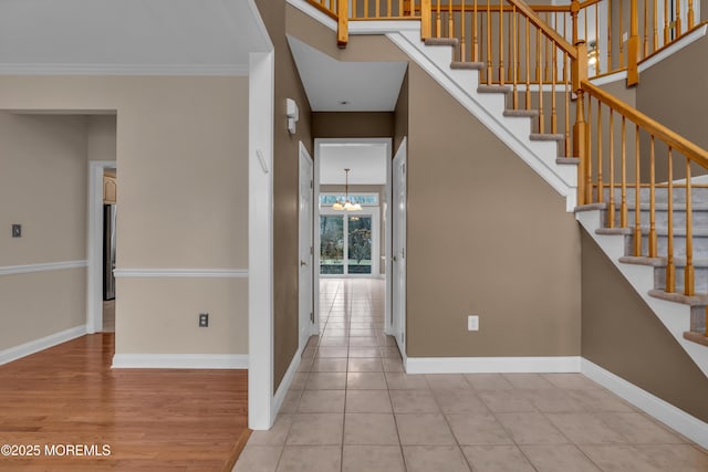 foyer featuring stairway, baseboards, a notable chandelier, and crown molding