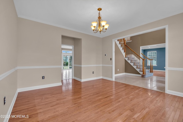 empty room with light wood-type flooring, a notable chandelier, stairway, crown molding, and baseboards