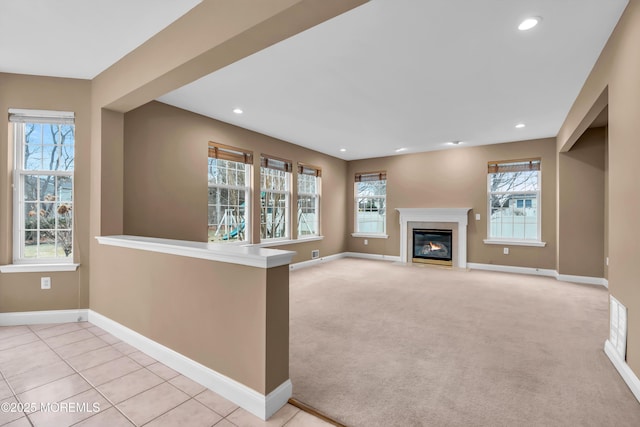 unfurnished living room featuring plenty of natural light, baseboards, a fireplace with flush hearth, and light carpet