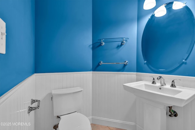 half bathroom featuring a wainscoted wall, toilet, and a sink