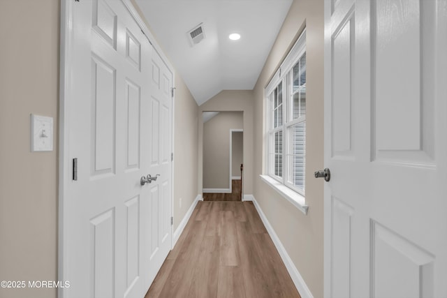 hall featuring visible vents, lofted ceiling, light wood-style floors, and baseboards