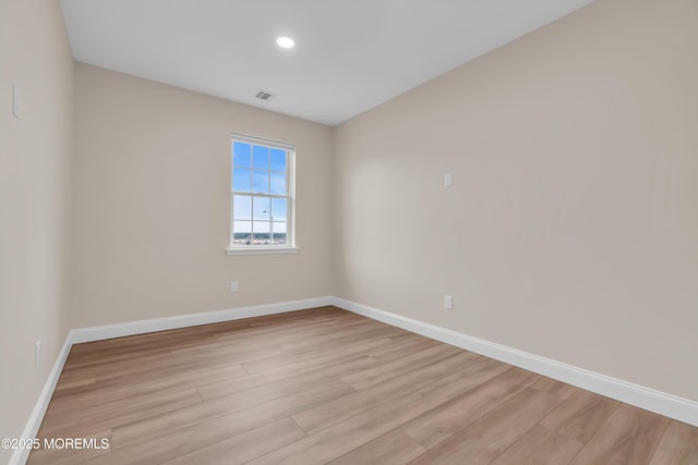 empty room with light wood-style floors, visible vents, and baseboards