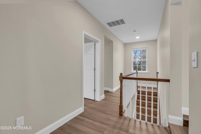 hallway with wood finished floors, an upstairs landing, visible vents, and baseboards